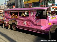 a pink bus with hello kitty painted on it's side driving down the street