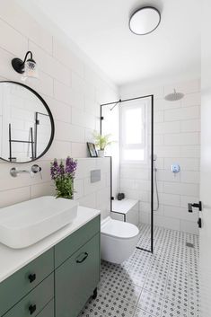 a white bathroom with black and white tile flooring, a round mirror above the sink