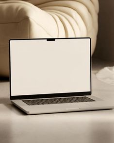 an open laptop computer sitting on top of a white table next to a beige couch