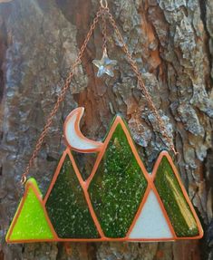 a stained glass sun catcher hanging on a tree branch with a crescent and mountains design