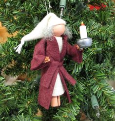 a doll ornament hanging from a christmas tree with a candle in its hand