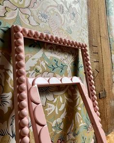 an ornate pink frame with beaded edges on a floral wallpaper