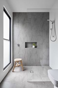 a modern bathroom with concrete walls and floor, along with a wooden stool in the foreground