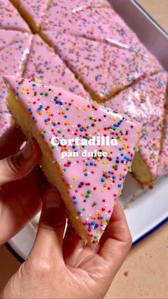 a person holding a piece of cake with pink frosting and sprinkles