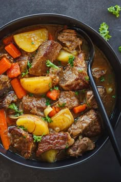 beef stew with carrots, potatoes and parsley in a black bowl on a dark surface