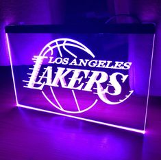 the los angeles lakers logo is illuminated in purple and white on a wooden table top