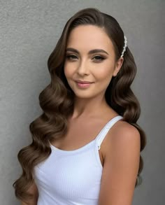 a woman with long brown hair wearing a white tank top and pearls in her hair