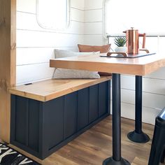 a wooden table sitting under a window next to a black and white rug on top of a hard wood floor