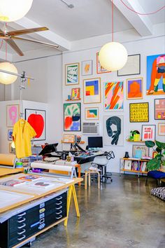 an art studio with lots of paintings on the wall and desks in front of them