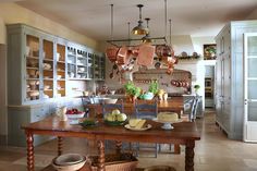 a kitchen with lots of wooden furniture and hanging pots on the wall above the table