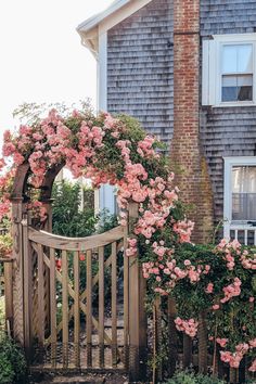 a wooden gate surrounded by pink flowers next to a house