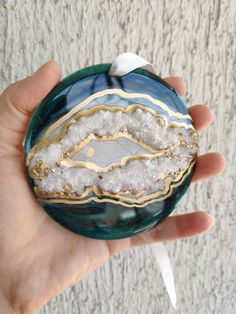 a hand holding a glass ornament with white and gold designs