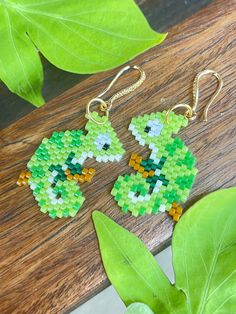 two green and yellow beaded earrings sitting on top of a wooden table next to leaves