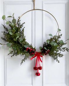 a wreath hanging on the front door with bells and greenery around it for christmas