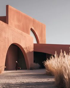 a person standing in front of a pink building with arches and doorways on the side