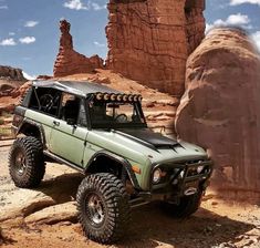 a green jeep parked in the desert near some rocks and large rock formations with blue skies above