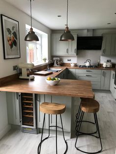 A sage green shaker kitchen with wooden worktops and wood and black bar stools. a light wooden floor is also shown.