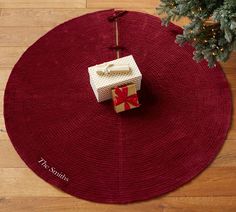 a red round rug with a present on it and a christmas tree in the corner