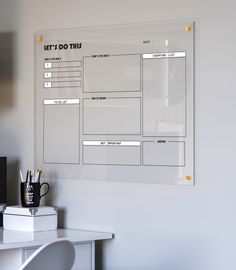 a dry erase board mounted to the side of a wall next to a white desk