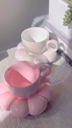 two pink cups sitting on top of a table next to a stack of books and magazines