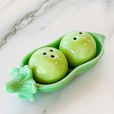 two peas in a pea pod shaped dish on a marble countertop, with the tops painted green