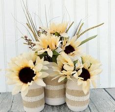 three vases with sunflowers in them sitting on a wooden table next to a white wall