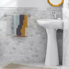 a white pedestal sink sitting next to a mirror in a bathroom with hexagonal tiles on the wall