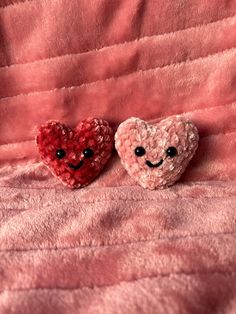 two little hearts with faces made out of sequins sitting on a pink blanket