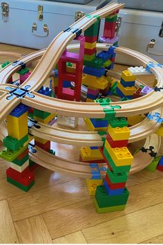 a wooden toy train set with lots of blocks on the tracks in front of a suitcase