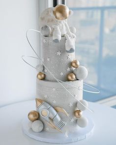 a three tiered cake decorated with silver and gold decorations on top of a white table