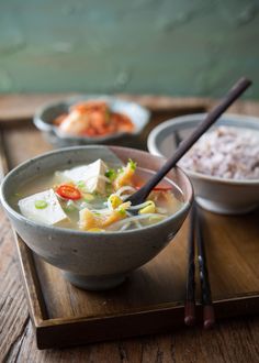 a bowl of soup with chopsticks and rice on a wooden tray next to another bowl