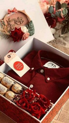 a red shirt and some wine bottles in a box with flowers on the table next to it