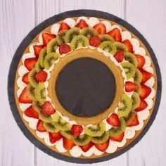 a pie with sliced kiwis and strawberries in the middle on a white wooden table