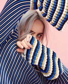 a woman with grey hair wearing blue and white striped shirt holding her hands over her face