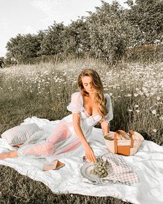 a woman sitting on top of a blanket next to a bowl of grapes in a field