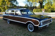 an old station wagon is parked on the grass in front of a white picket fence