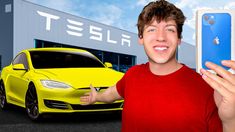 a man holding up a cell phone in front of a yellow car and a tesla dealership