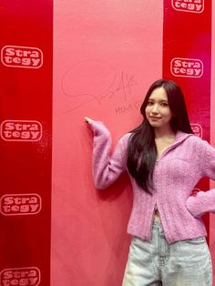 a woman standing in front of a pink wall with writing on it and pointing to the side