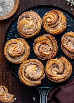 several cinnamon rolls on a black plate with powdered sugar around them and two wooden spoons