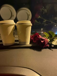 three coffee cups sitting on top of a car dashboard next to a red rose and two white paper cups