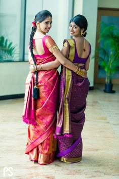 two women standing next to each other in colorful sari dresses, one holding the other's hand