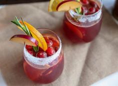 two glasses filled with fruit and garnish on top of a cloth covered table