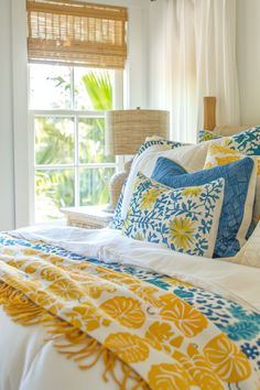 a bed with yellow, blue and white pillows on top of it next to a window