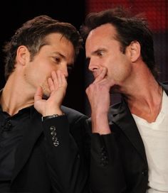 two men sitting next to each other and one is touching his face with his hand