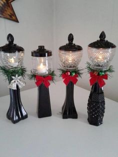 three black vases with red bows and pine cones are sitting on a white table