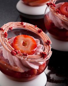 two desserts with strawberries and whipped cream in them on a black counter top