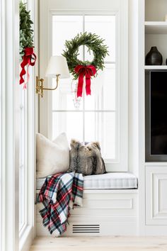 a window seat with a christmas wreath hanging on it's side and a plaid blanket draped over it