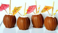 four chocolate covered candy apples with umbrellas sticking out of the top, on a white surface