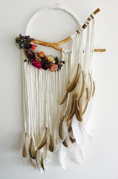 a white wall hanging with feathers and flowers on the side, along with a twig