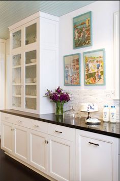 a kitchen with white cabinets and black counter tops in front of pictures on the wall